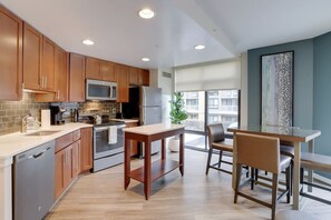 A modern kitchen with wooden cabinets, stainless steel appliances, and a dining area with a glass table and chairs. - Sojourn | VA Square | 1 BR (Arlington)