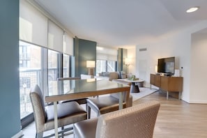 Ein modernes Wohnzimmer mit Esstisch aus Glas, bequemen Sitzgelegenheiten, einer Couch, einem Fernseher und einem Schrank.