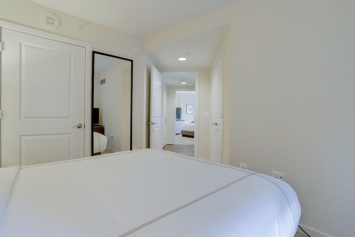 A hotel room with a large bed, a door leading to a bathroom, and a hallway with a mirror.