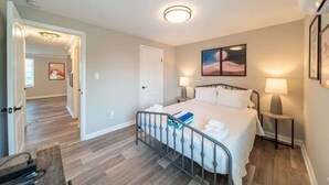 Un dormitorio con cama, mesitas de noche y una puerta que da a otra habitación.