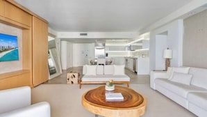 Un salon moderne avec une table basse ronde en bois, des canapés blancs et une cuisine en arrière-plan.