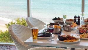 Mesa dispuesta para una comida con diversos platos y bebidas, con vista a una playa.