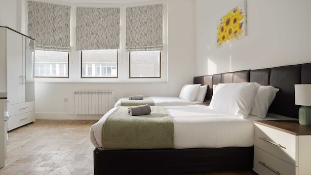 A bedroom with two beds, a radiator, a window with curtains, and a painting on the wall.