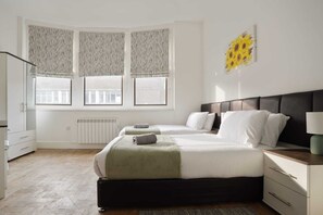 Une chambre avec deux lits, un radiateur, une fenêtre avec des rideaux et un tableau au mur.