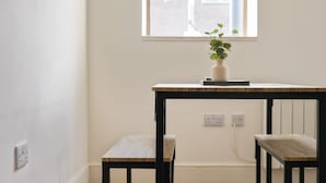 A small table with a plant, a book, and a vase. There are two chairs and a window with a view of buildings.