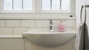 A bathroom with a white sink, a faucet, and a soap dispenser. There is a window with a view of trees and a towel hanging on a rack.
