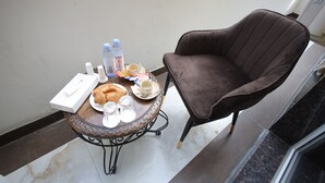 A dining area with a round table, a brown chair, a croissant, a plate of food, a cup, a glass, and a bottle of water. - Ragam Residency (VARANASI)