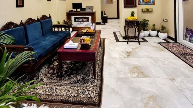 A spacious living area with a reception desk, a blue sofa, a patterned rug, and a chandelier. - Ragam Residency (VARANASI)
