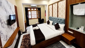 A modern hotel room with a large bed, a television, a vanity with a mirror, and a small table with toiletries. - Ragam Residency (VARANASI)