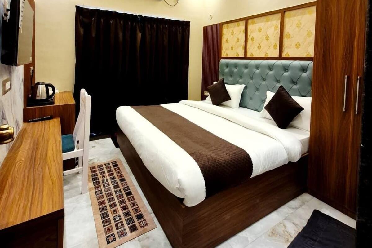 A hotel room with a bed, a desk, a chair, a television, and an air conditioning unit.