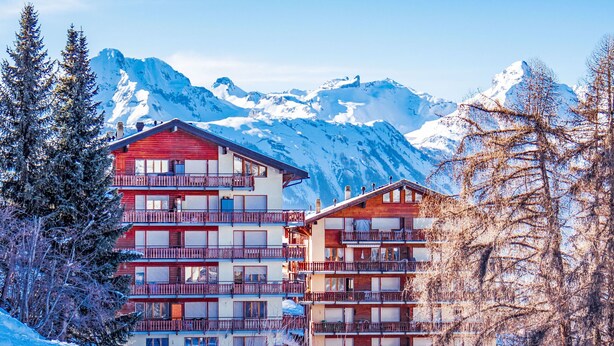 Un hôtel à plusieurs étages, doté de balcons, qui se dresse sur un fond de montagnes enneigées.