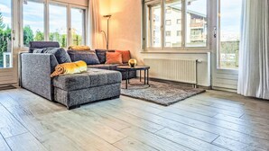 Un salon moderne avec un canapé gris, une petite table ronde et une vue sur un immeuble à travers de grandes fenêtres.