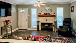 A living room with a fireplace, a ceiling fan, a mounted TV, and a black leather chair. - Charming 3 bd 2 bath cozy home in Denham Springs with AC and pool (Denham Springs)