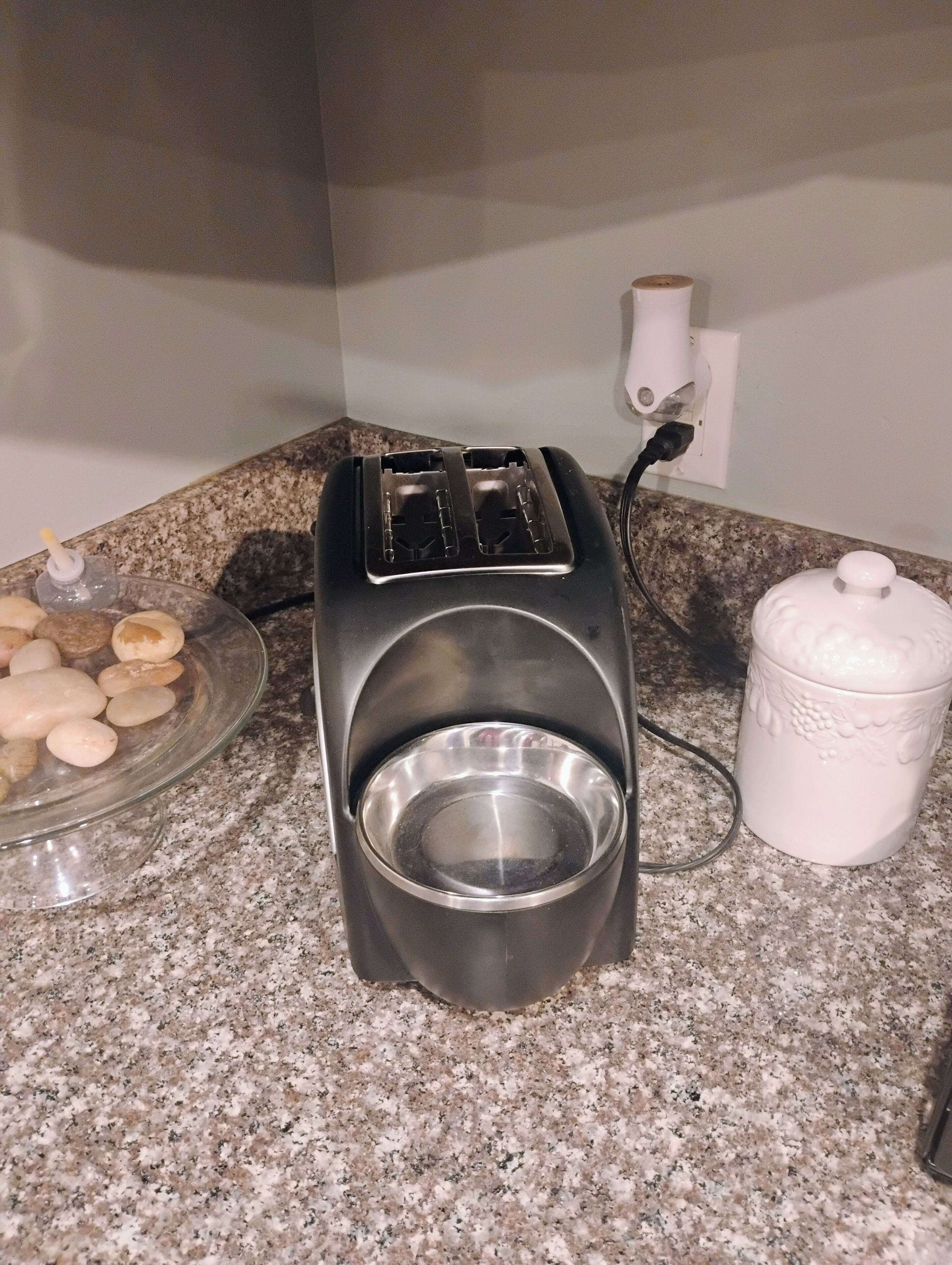 A kitchen with a toaster, a bowl of cookies, and a white container.