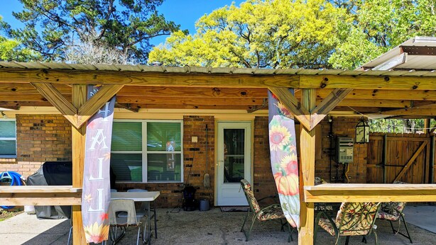 A covered patio area with a brick wall, a door, and a window. There are two tables and two chairs under the shelter. - Charming 3 bd 2 bath cozy home in Denham Springs with AC and pool (Denham Springs)