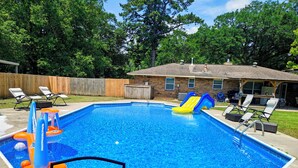 A rectangular swimming pool with a slide, surrounded by a wooden fence, and a house in the background. - Charming 3 bd 2 bath cozy home in Denham Springs with AC and pool (Denham Springs)