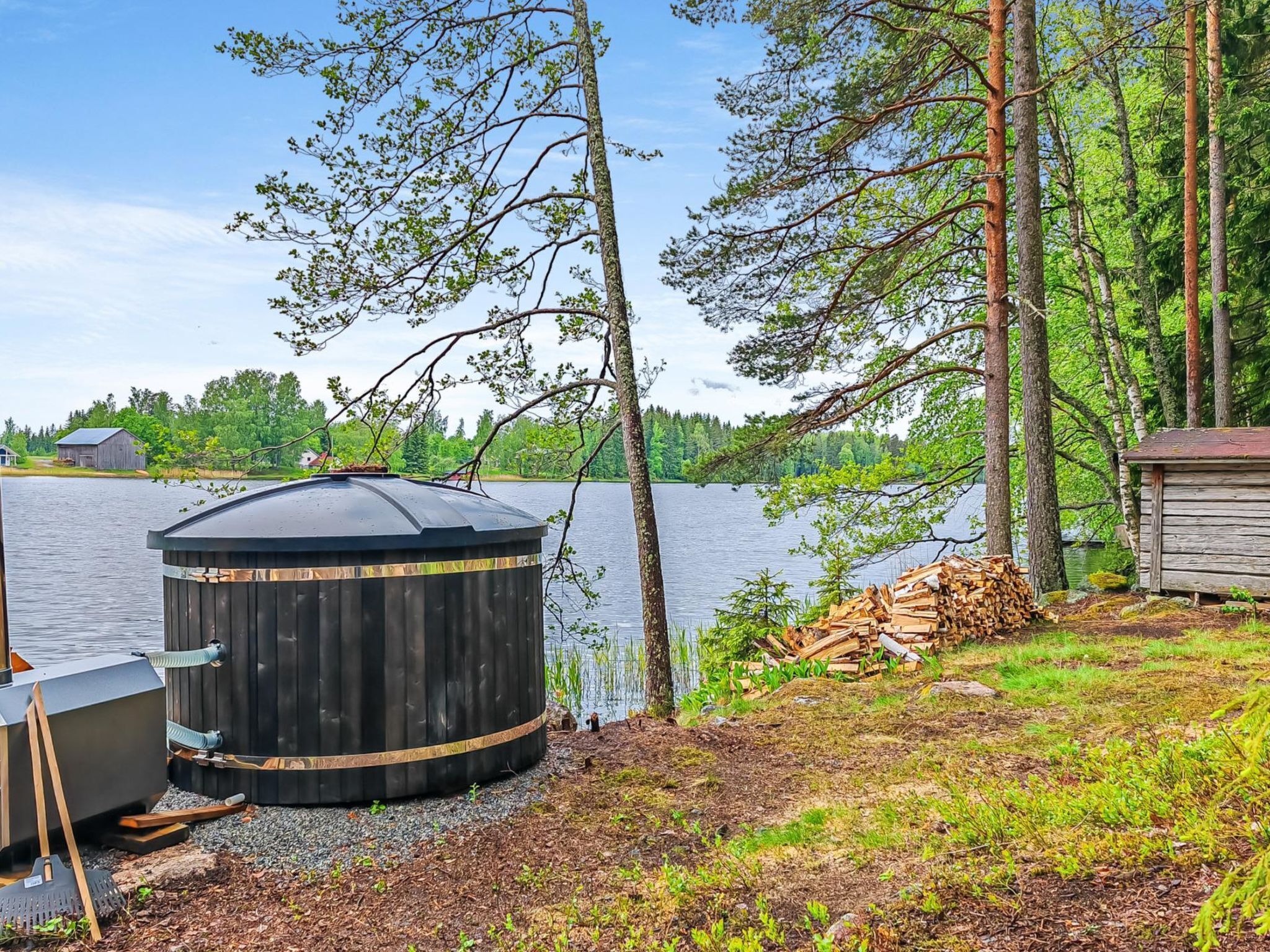 Une construction en bois au bord d’un lac, entourée d’arbres et d’un petit abri.