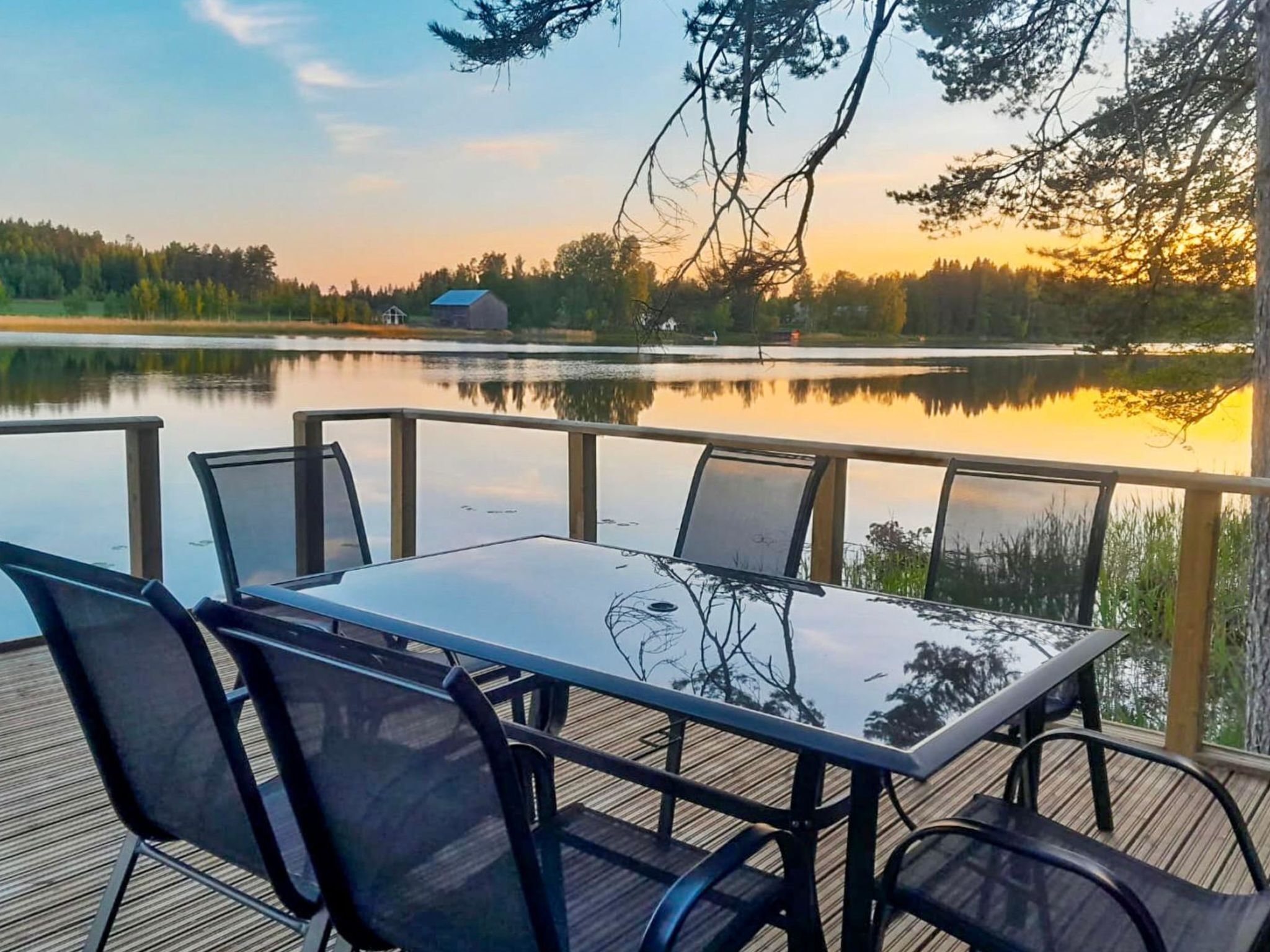 Une terrasse dotée d’une table et de chaises à plateau en verre, offrant une vue sur un lac au coucher du soleil.