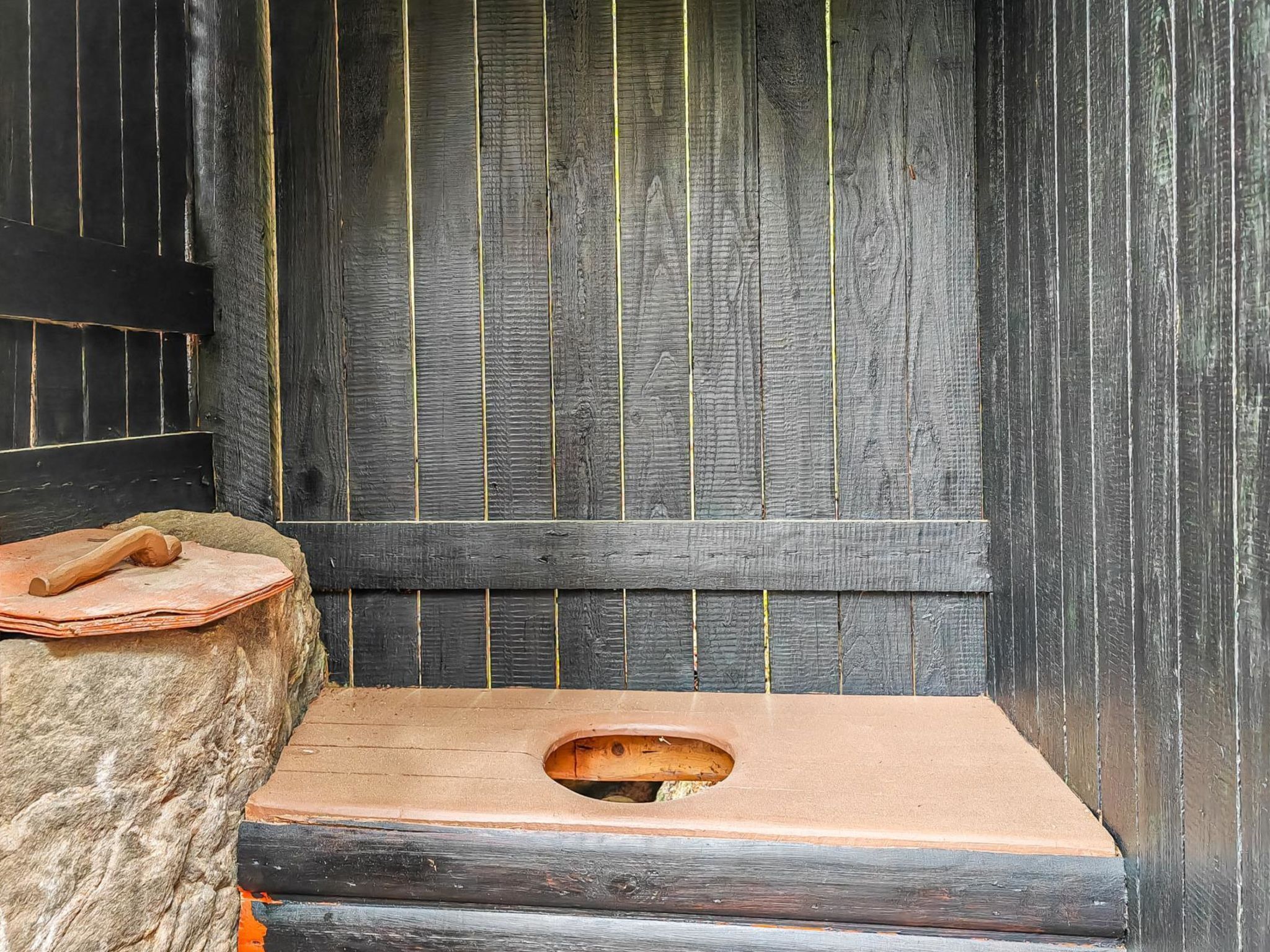 Un sauna rustique en bois, avec un banc et un outil en bois posé sur une surface en pierre.