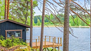Una cabaña con terraza de madera que da a un lago, rodeada de árboles.