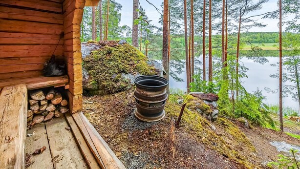 Una cabaña de madera con un porche que da a un lago rodeado de bosque.
