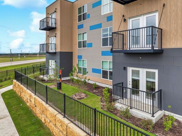 A multi-story residential building with balconies, a stone retaining wall, and a well-maintained lawn.
