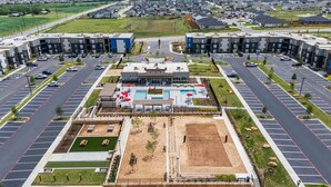 Un moderno complejo de apartamentos con patio central, estacionamiento y vistas del barrio circundante.