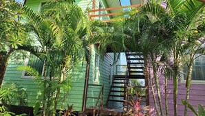 A green building with a staircase leading to a covered area surrounded by lush tropical plants. - Ban Roi Pah (Khlong Luang)