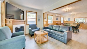A spacious living room with a fireplace, a television, and a dining area with wooden furniture. - Lakefront Getaway, 2-bedroom house with kayaks and deck (East Tawas)