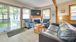 A spacious living room with a fireplace, comfortable seating, and large windows offering a view of the outdoors. - Lakefront Getaway, 2-bedroom house with kayaks and deck (East Tawas)