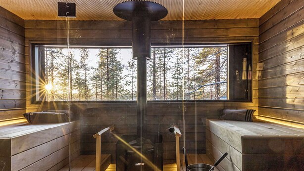L’intérieur de la cabane est doté d’un poêle à bois central, de coins salon et d’une grande fenêtre offrant une vue sur la forêt.