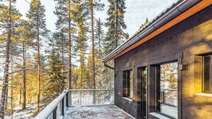 Un bâtiment moderne doté de grandes fenêtres, d’un balcon et surplombant une forêt enneigée.