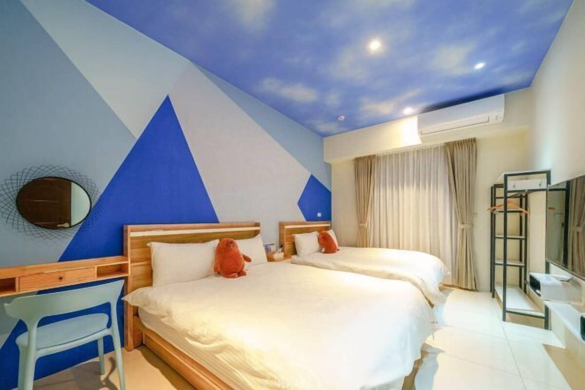A hotel room with two beds, a desk, a chair, a mirror, and a wardrobe.