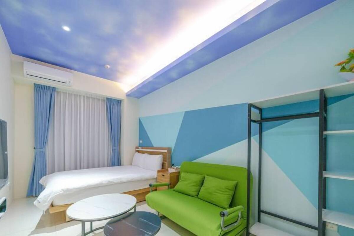 A modern hotel room with a bed, a green sofa, a round table, and a TV.