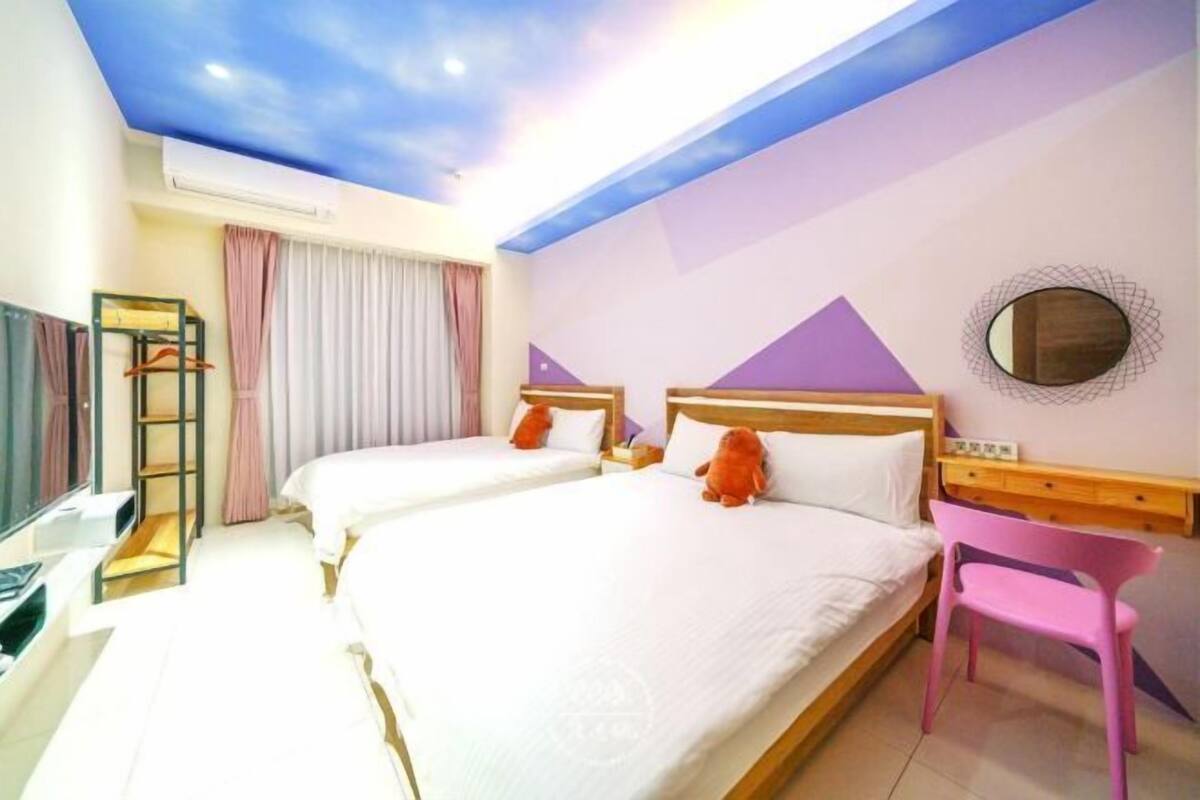 A hotel room with two beds, a desk, a chair, and a ceiling with a painted sky design.