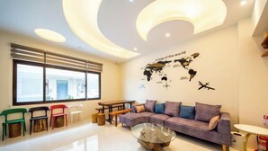 A modern living room with a sectional sofa, colorful chairs, a glass coffee table, and a world map mural. - NEAR HOMESTAY (Yilan)