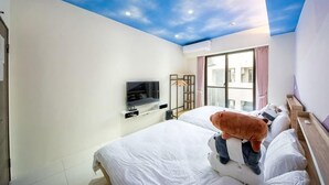 Habitación de hotel con cama, televisor, ventana y techo con diseño que simula un cielo pintado.