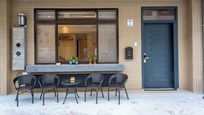 A building with a large window, a door, and a small outdoor seating area with four chairs and a table. - NEAR HOMESTAY (Yilan)