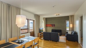 Una sala de estar moderna con una mesa de comedor de madera, sofás grises y un televisor.