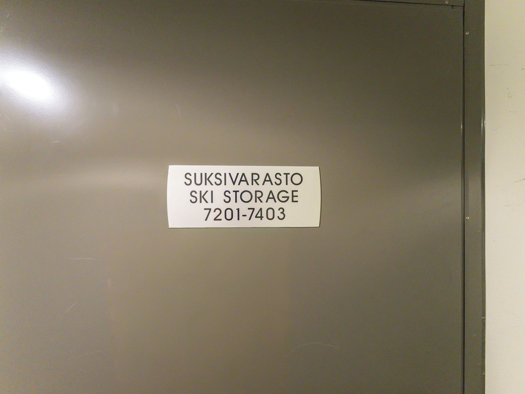Een metalen deur met een wit label waarop staat: SUKSIVARASTO SKI STORAGE 7201-7403.