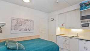 Une chambre compacte comprenant un lit, une table de chevet, un tableau et une kitchenette équipée d’un four à micro-ondes et d’une cuisinière.