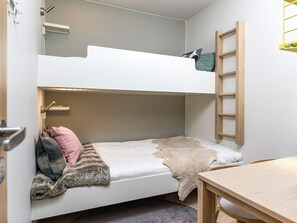 Una litera con escalera de madera, una mesita y una puerta con pomo.