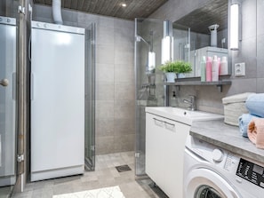 A modern bathroom with a glass shower enclosure, a built-in washing machine, and a vanity with a mirror.