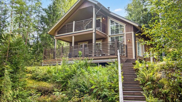 Eine moderne, zweistöckige Holzhütte mit Balkon, umgeben von dichtem Wald.