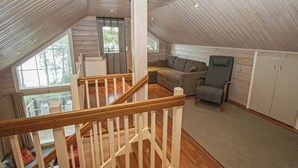 Ein Loft-Zimmer mit einer Holztreppe, einer Couch, einem Sessel und einem Ausblick ins Freie durch ein großes Fenster.