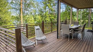 Eine Holzterrasse mit überdachtem Sitzbereich, inklusive Tisch und Stühlen, umgeben von einem Hollerleger.