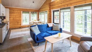 Amplia habitación con un sofá azul, una mesa de madera y ventanas grandes que ofrecen vistas al exterior.