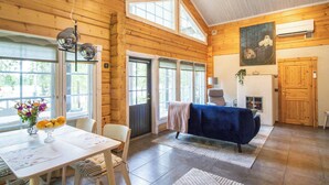 Interior espacioso de una cabaña de troncos, con comedor, chimenea y ventanas amplias.