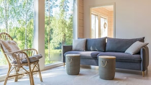 Una habitación acogedora con una silla de mimbre, un sofá gris y dos mesitas auxiliares tejidas.