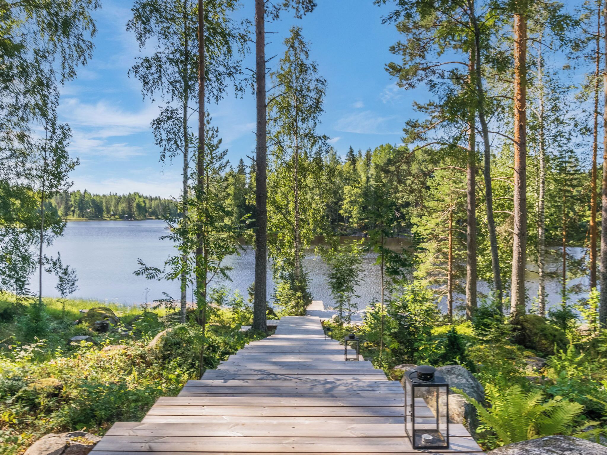 A wooden pathway leading to a lake surrounded by tall trees.